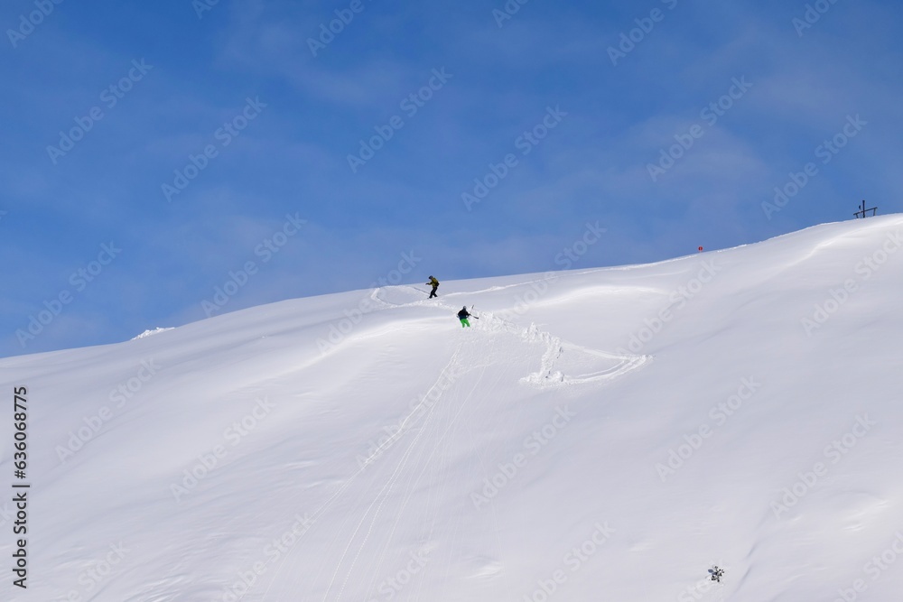 Pair of off-piste skiers climbing back up after a wrong turn whilst backcountry skiing in the Austrian alps.