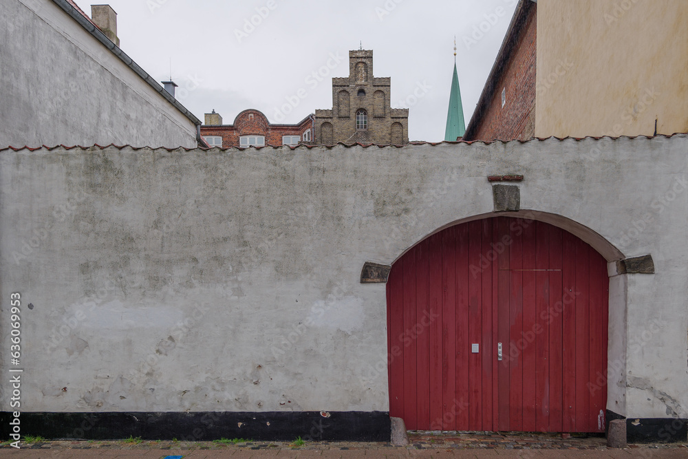 Φωτογραφία Outdoor exterior street view at wooden red arch door and old dirty rough white painted wall against overcast sky