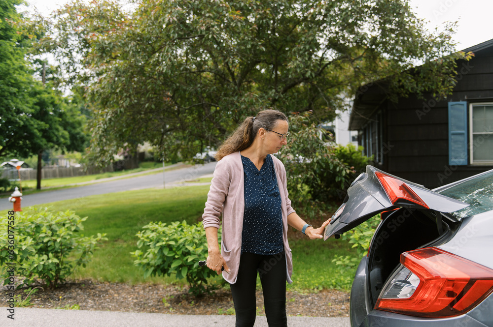 woman shutting the trunk of her sedan car in her driveway woman shutting the trunk of her sedan car in her driveway