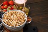 Tasty granola served with fresh berries, nuts and honey on wooden table, space for text. Healthy breakfast
