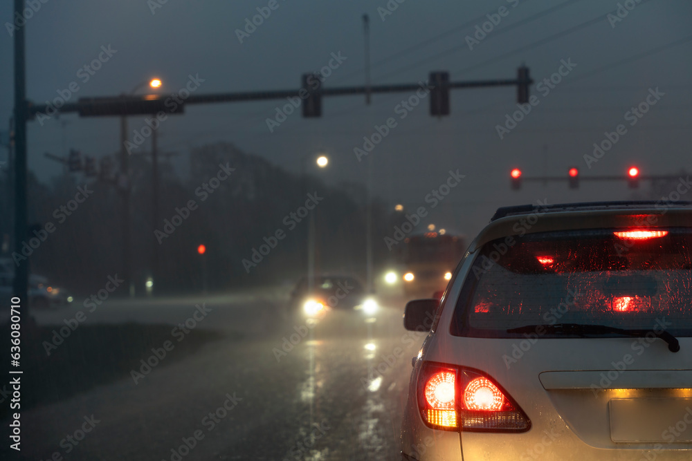 Cars driving at rainy night at traffic lights on american wide road intersection in city area. Transportation system in USA