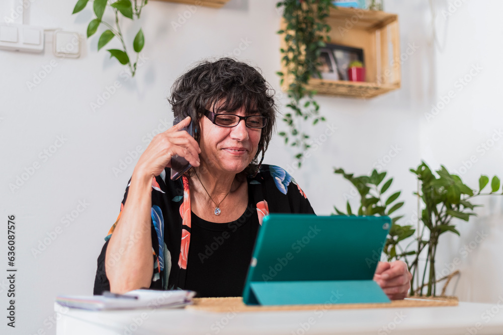 Mature woman talking on the phone using tablet at home