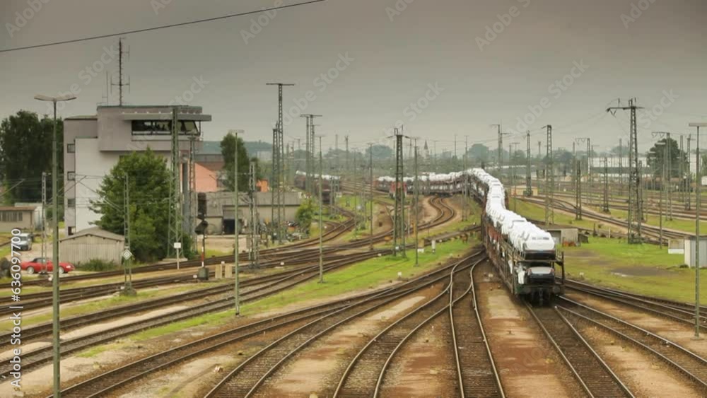 Handheld camera from an elevated view captures a train yard bustling with trains filled with white cargo cars, control tower on the left, encircled by verdant trees under an overcast sky Handheld camera from an elevated view captures a train yard bustling with trains filled with white cargo cars, control tower on the left, encircled by verdant trees under an overcast sky