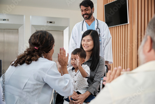 Happy young female pediatric doctor in uniform teasing little boy in wheelchair for medical exam at outpatient clinic hospital, people public health care checkup, and appointment visit.