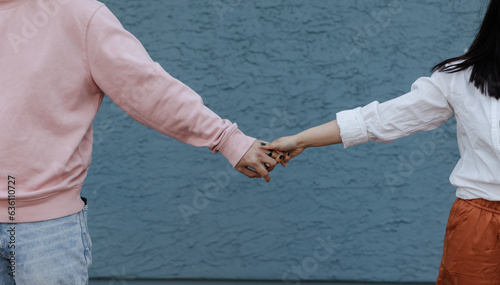 Anonymous couple holding hands and pulling apart with blue wall  photo