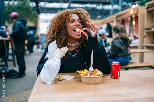 Happy black lady biting fast food in street cafe photo