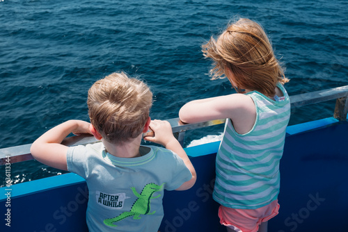 Two young kids look over the side of a boat at sea