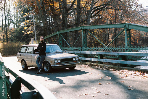 millennial man standing by his old classic car outdoors in autumn