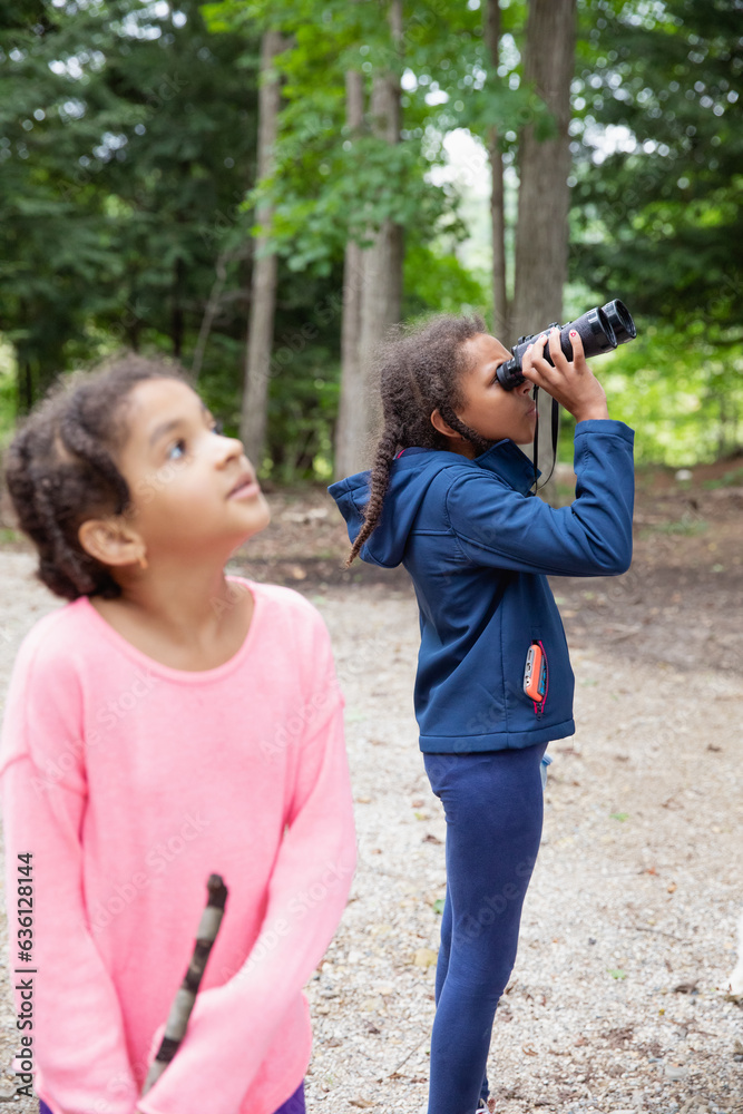 Child looking through a pair of binoculars as her sister stands nearby Child looking through a pair of binoculars as her sister stands nearby
