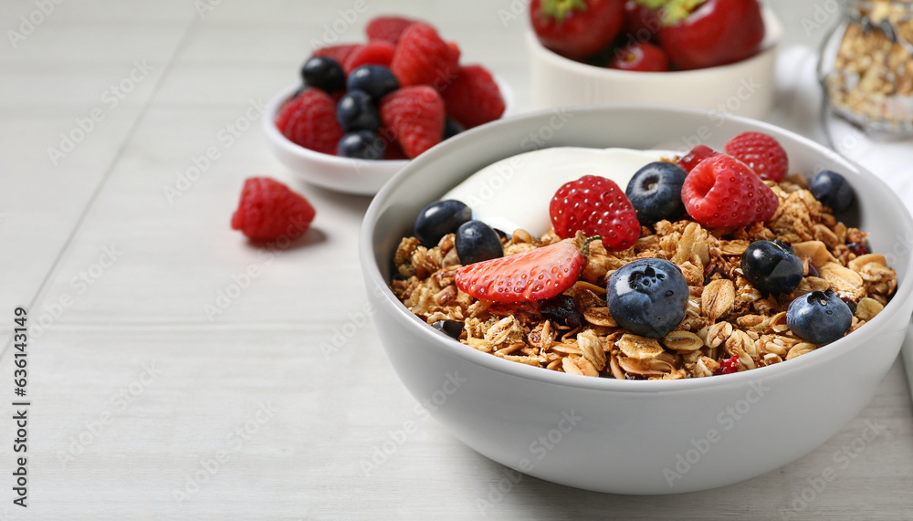 Tasty granola, yogurt and fresh berries in bowl on white tiled table, closeup with space for text. Healthy breakfast