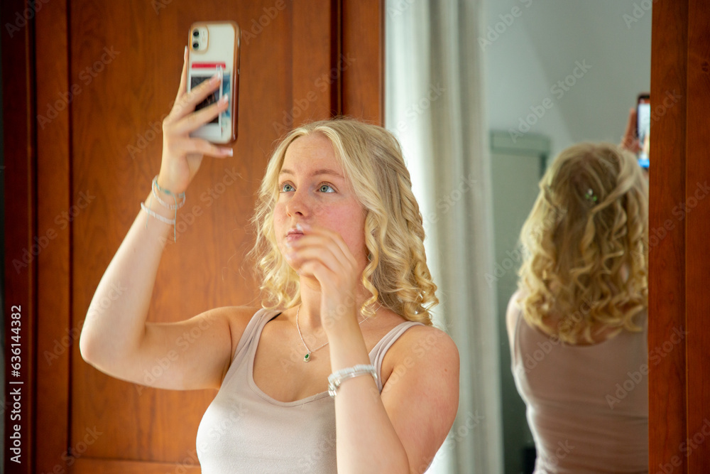 Blonde teenage girl checking her hair in a mirror Stock Photo | Adobe Stock
