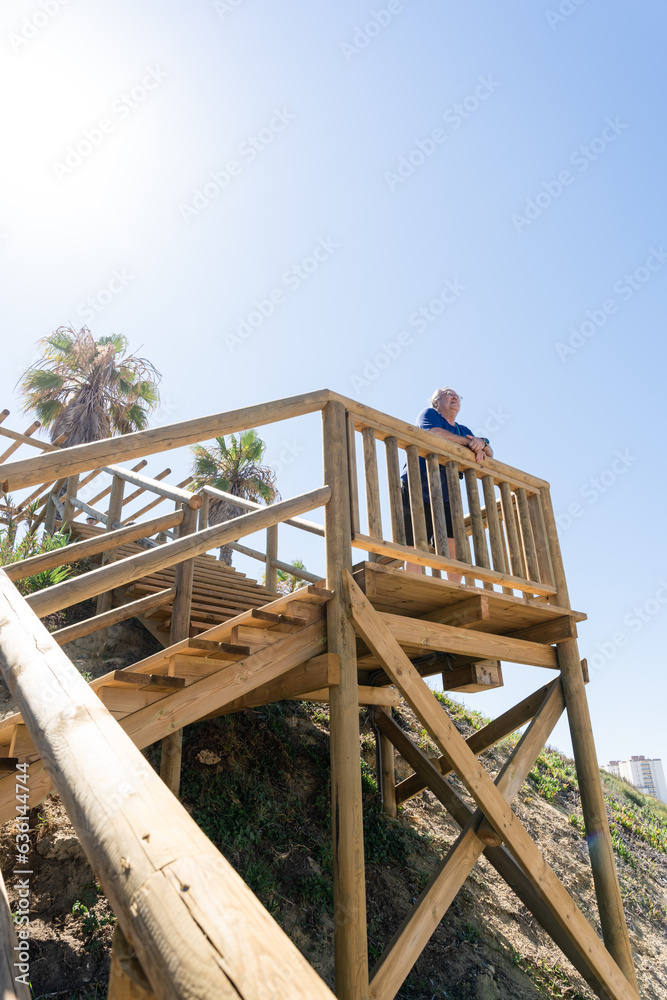 senior man gazing at the sea from a wooden boardwalk senior man gazing at the sea from a wooden boardwalk