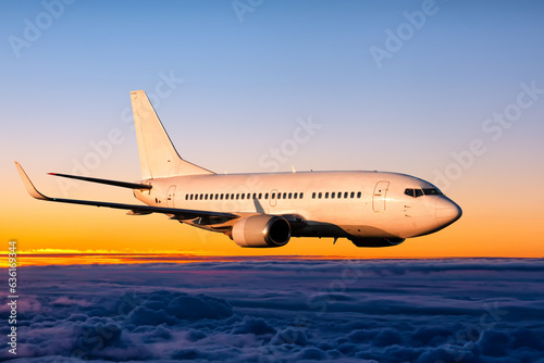 White passenger airplane is flying in the sunrise sky