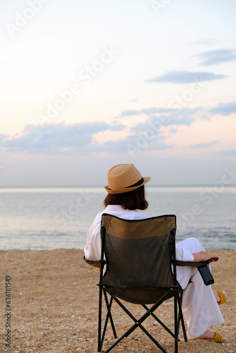 a fasion woman is sitting on tourist chair and looking at sea. © Di_Ilikaeva