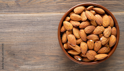 Almonds in brown bowl on textured wooden background, top view. Copy space on left side