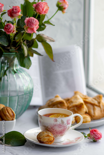 An elegant tea pair, homemade sweet pastries and a bouquet of pink roses in a turquoise glass vase. Stylish tea party in English style