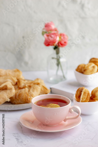 An elegant tea pair, homemade sweet pastries and a bouquet of pink roses in a turquoise glass vase. Stylish tea party in English style