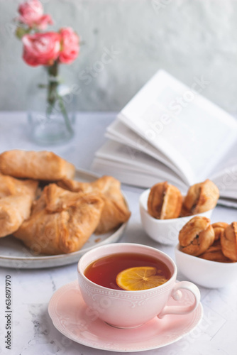 An elegant tea pair, homemade sweet pastries and a bouquet of pink roses in a turquoise glass vase. Stylish tea party in English style