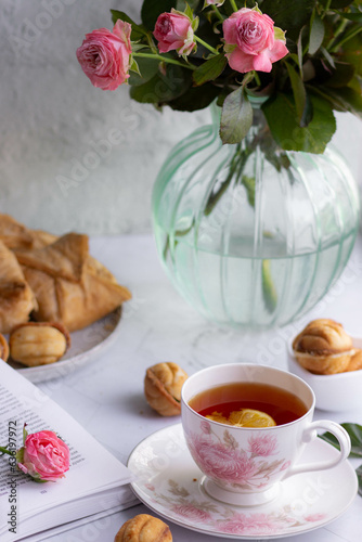 An elegant tea pair, homemade sweet pastries and a bouquet of pink roses in a turquoise glass vase. Stylish tea party in English style