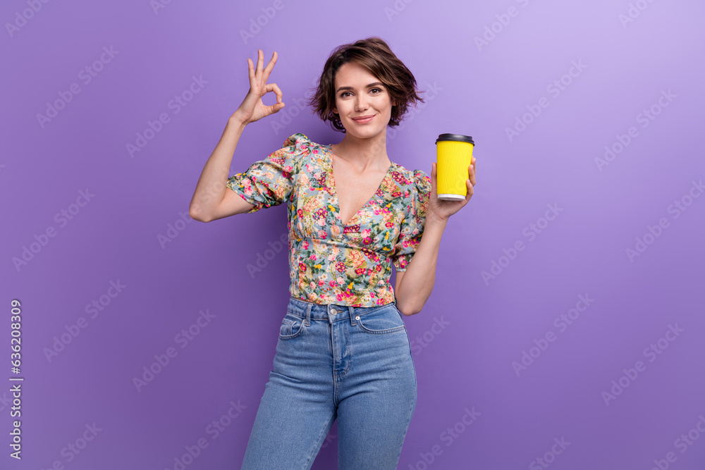 Photo portrait of attractive young woman show okey sign paper cup dressed stylish flower print clothes isolated on purple color background Photo portrait of attractive young woman show okey sign paper cup dressed stylish flower print clothes isolated on purple color background