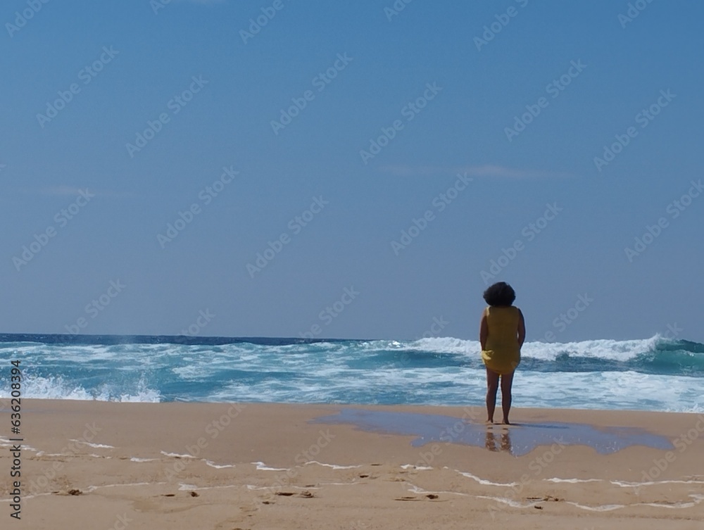 A woman stands alone on the beach and looks out over the ocean. Space for text