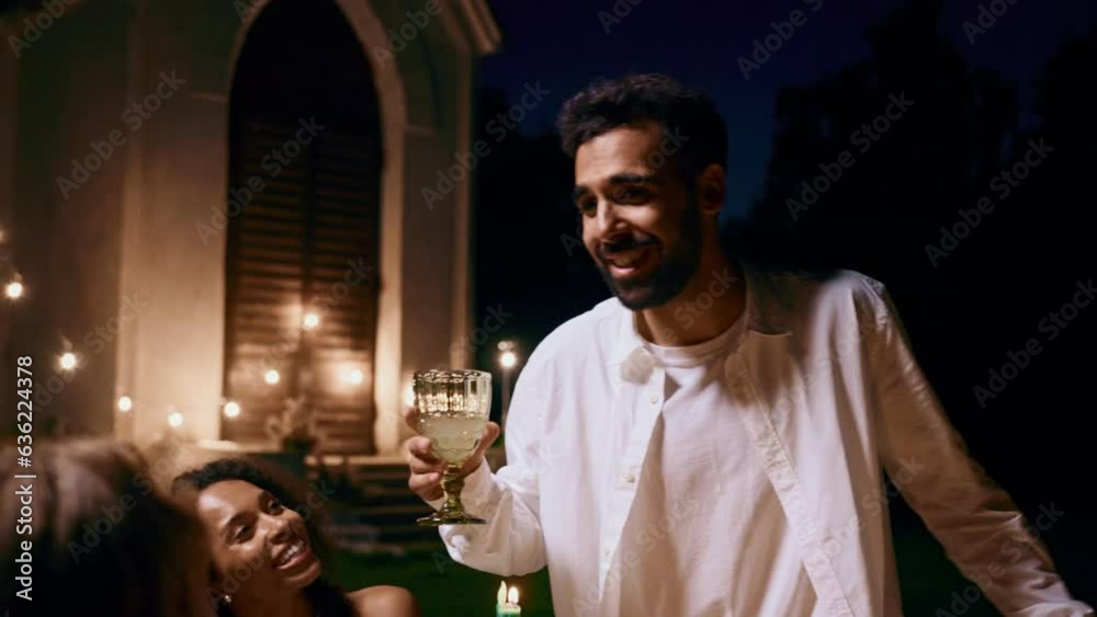 A man makes a toast standing up from the festive table with a glass in his hands at an outdoor party at night A man makes a toast standing up from the festive table with a glass in his hands at an outdoor party at night
