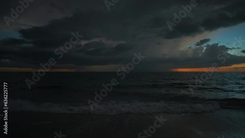 Sunset landscape of dark ominous rainstorm with lightning and thunder over sea water waves crushing on sandy beach. Beautiful seascape in evening photo