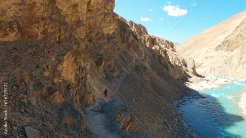 4K shot of an Indian man walking on the hiking trail towards the Phugtal monastery besides the blue Tsarap chu river at Zanskar valley in Ladakh, India. Man trekking towards the Phugtal gompa. photo