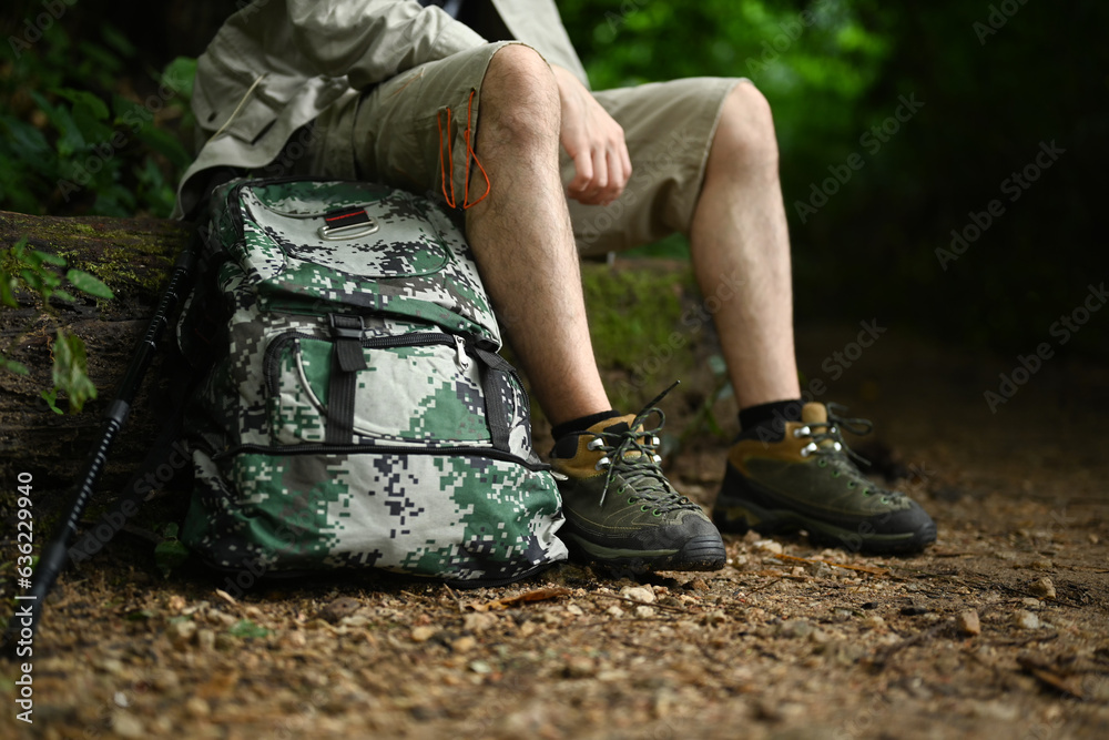 Unrecognizable man with backpack sitting on rocks resting during hiking in green forest. Traveling, trekking and adventure concept.