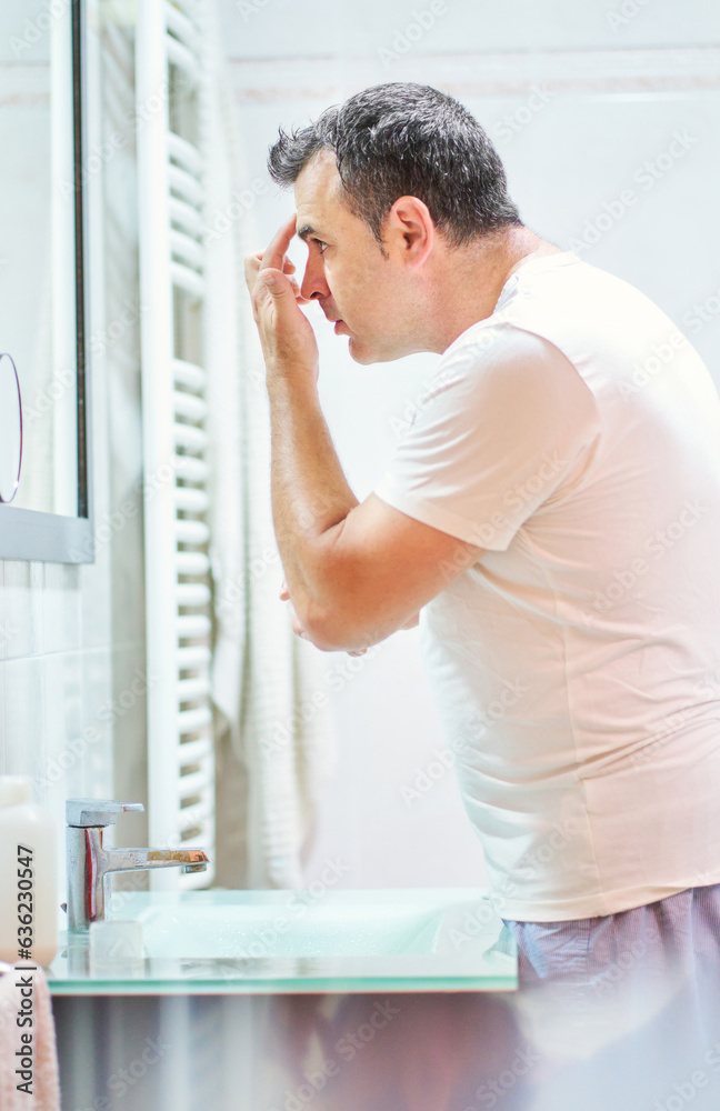 Man touching face in bathroom while looking in mirror