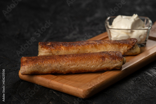 Fried pancakes with sour cream on a wooden board. Dark background