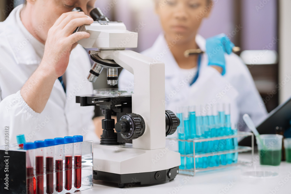 Team of biochemical research scientists working with a microscope for vaccine development in pharmaceutical research labeling. Team of biochemical research scientists working with a microscope for vaccine development in pharmaceutical research labeling.