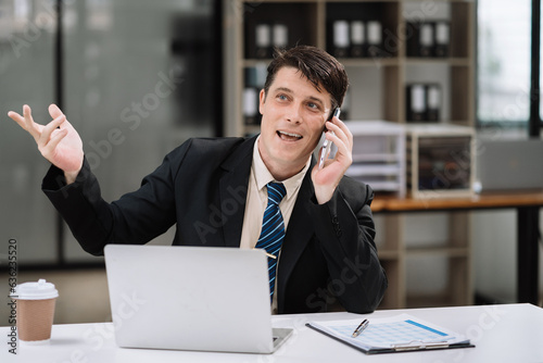 Businessman caucasian involved in cellphone call conversation working on computer, giving professional consultation to client or negotiating project.