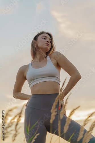 Fototapeta Naklejka Na Ścianę i Meble -  Female Fitness Trainer on the sand beach sunset background.  Meditation and harmony and balance of a person, mental health.     Practicing yoga exercises asana.