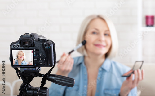 Woman doing makeup demonstrating cosmetics and shooting herself on video camera in studio