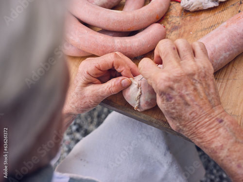 Fotografie Crop senior woman sewing sausage casing of pork guts