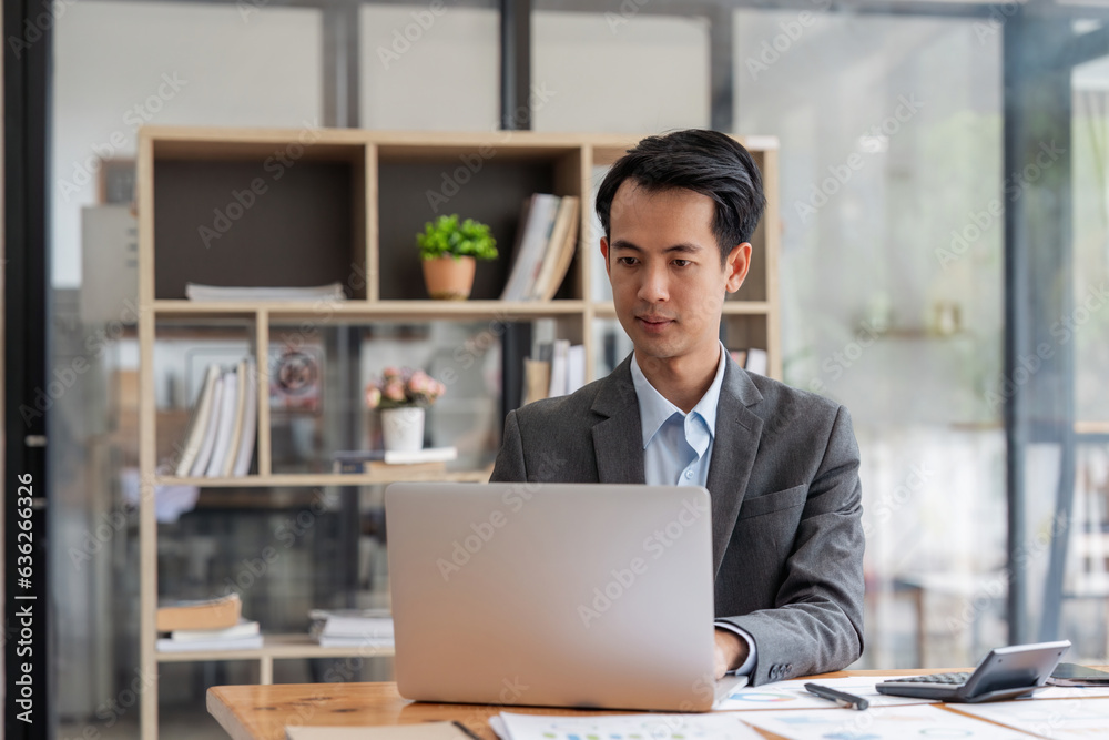 Asian businessman works in the office, calculate the report, the financial on paperwork, uses the laptop and the calculator Asian businessman works in the office, calculate the report, the financial on paperwork, uses the laptop and the calculator