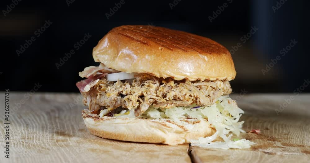 A burger with bread, barbecue sauce, coleslaw, pulled meat, onion rings and bacon is presented rotating. A burger with bread, barbecue sauce, coleslaw, pulled meat, onion rings and bacon is presented rotating.