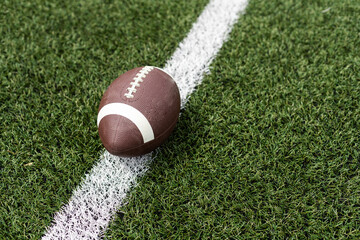 Close up view of an American Football sitting on a grass football field on the yard line. Generic Sports image 