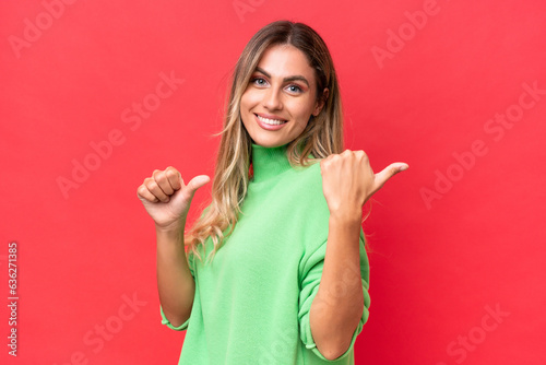 Young Uruguayan woman isolated on red background pointing to the side to present a product