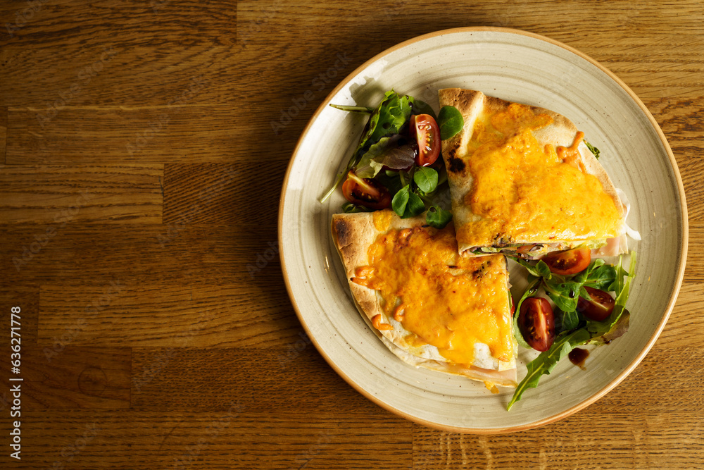 Ham and cheese tortilla sandwich with vegetables on a wooden table Ham and cheese tortilla sandwich with vegetables on a wooden table