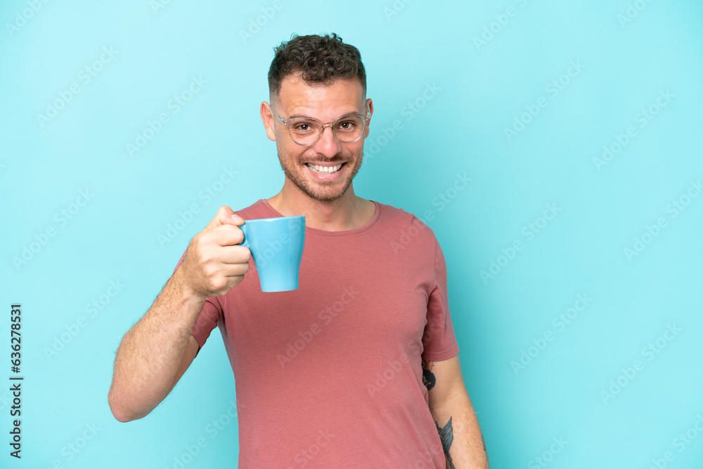 Young caucasian man holding cup of coffee isolated on blue background with happy expression Young caucasian man holding cup of coffee isolated on blue background with happy expression