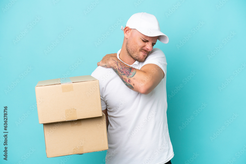Delivery caucasian man isolated on blue background suffering from pain in shoulder for having made an effort Delivery caucasian man isolated on blue background suffering from pain in shoulder for having made an effort
