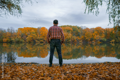 a man stands on the bank of the river and enjoys the scenery, beautiful nature in the autumn season, the river and the forest with bright yellow leaves, cloudy sky in the evening © soleg