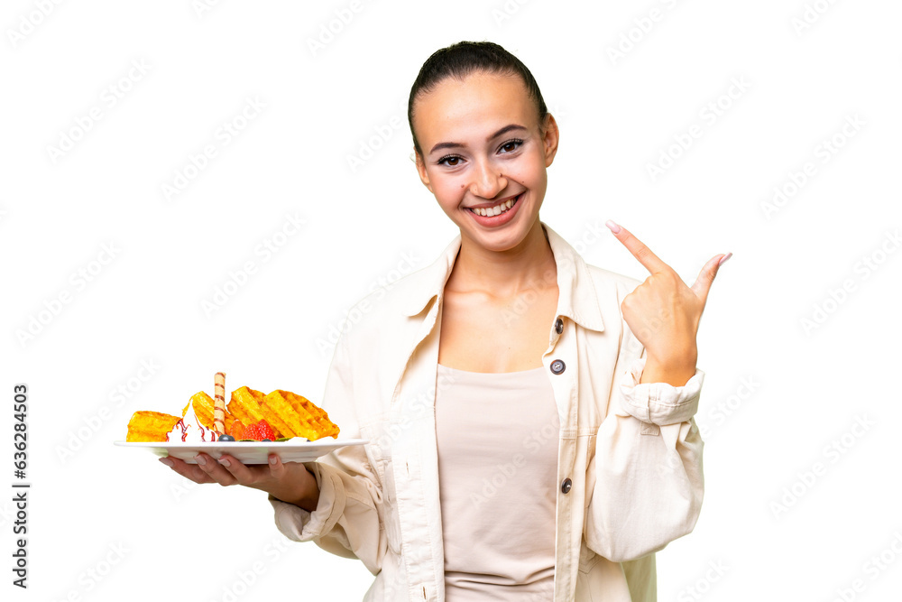 Young Arab woman holding waffles over isolated background giving a thumbs up gesture Young Arab woman holding waffles over isolated background giving a thumbs up gesture