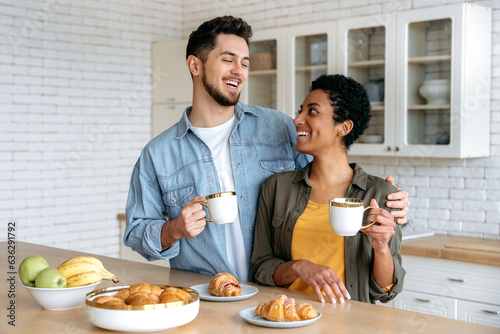 Morning coffee. Happy couple in love in the morning. Multiracial spouses have tasty weekend breakfast in the kitchen at home with croissants and coffee, spend time together, communicate, smile
