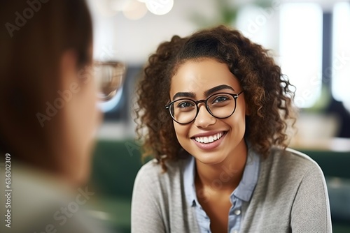 Smiling female curly haired patient with glasses looking at her psychologist, having consultations in the office interior. Mental health concept.