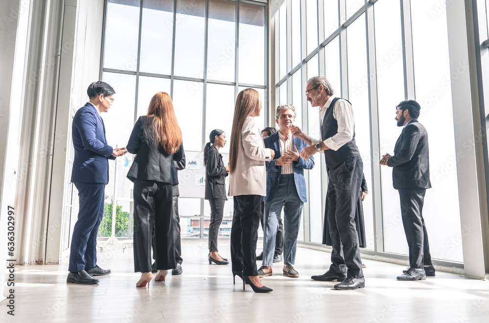 Group of multinational executives, men and women in suits, standing and talking, exchanging ideas, sharing business ideas in a conference room.