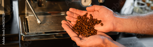 cropped view of barista holding coffee beans near blurred coffee machine in cafe, banner