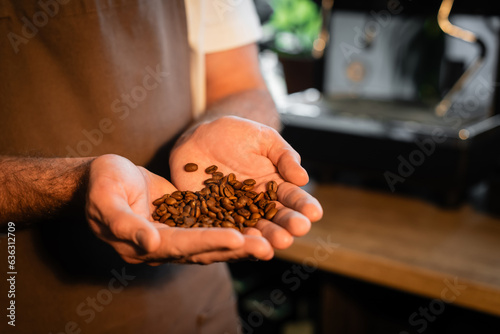 Cropped view of barista in apron holding coffee beans while working in blurred coffee shop